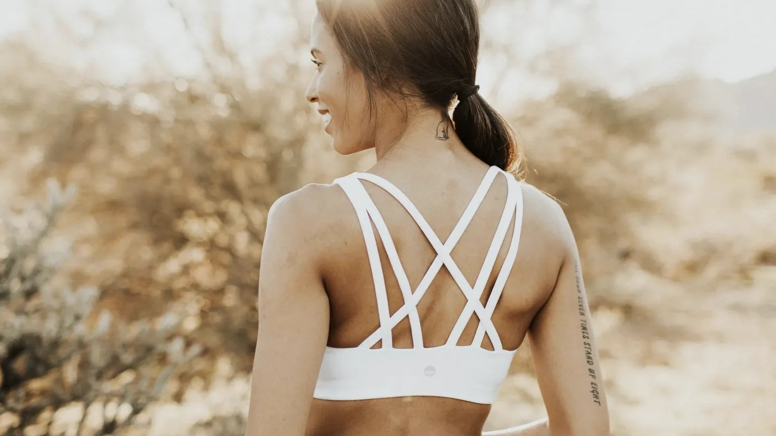 Woman in a desert setting with grey leggings showing the Strappy Sports Bra - White