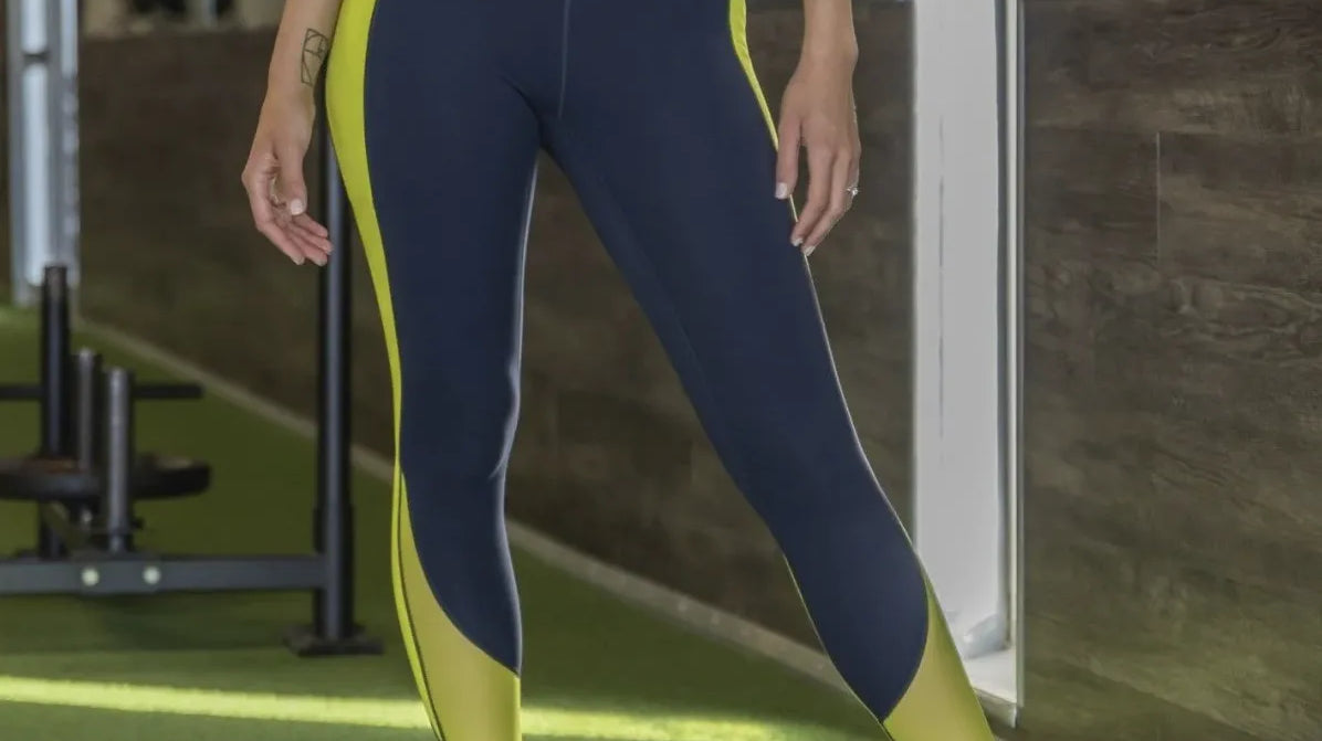 Woman wearing Skin Barre Mesh Leggings - Navy/Margarita standing in front of gym equipment