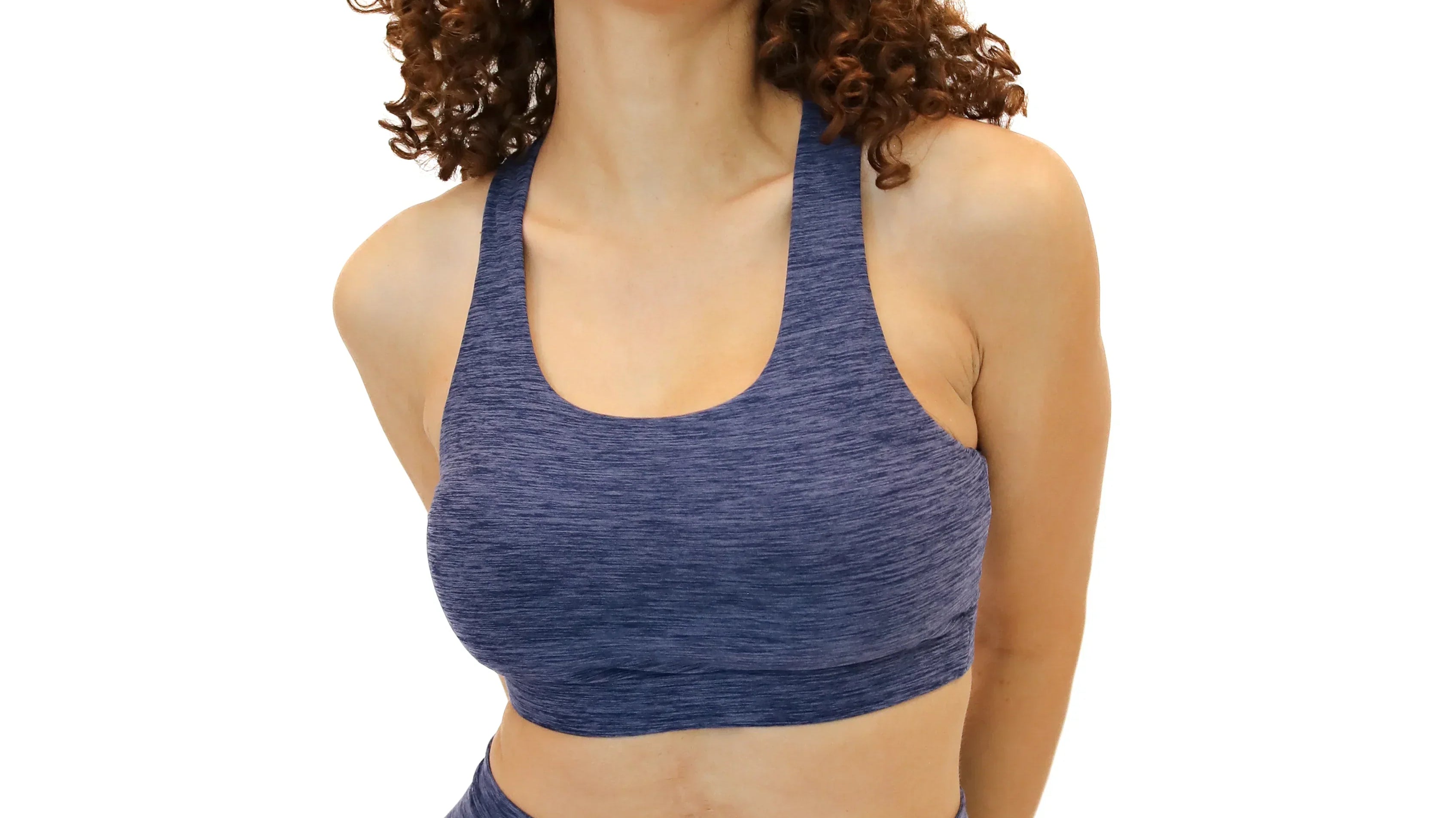 Front view of a smiling woman with curly brown hair wearing a scoop-neck, racerback sports bra and matching high-waisted leggings in a heathered navy blue fabric.