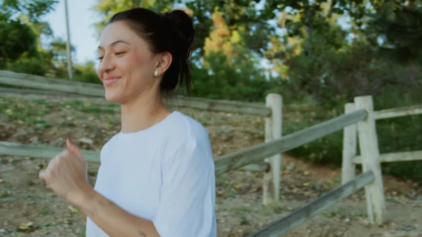 Woman smiling and running with Easy Tee - White, with wooden fence and trees in the background