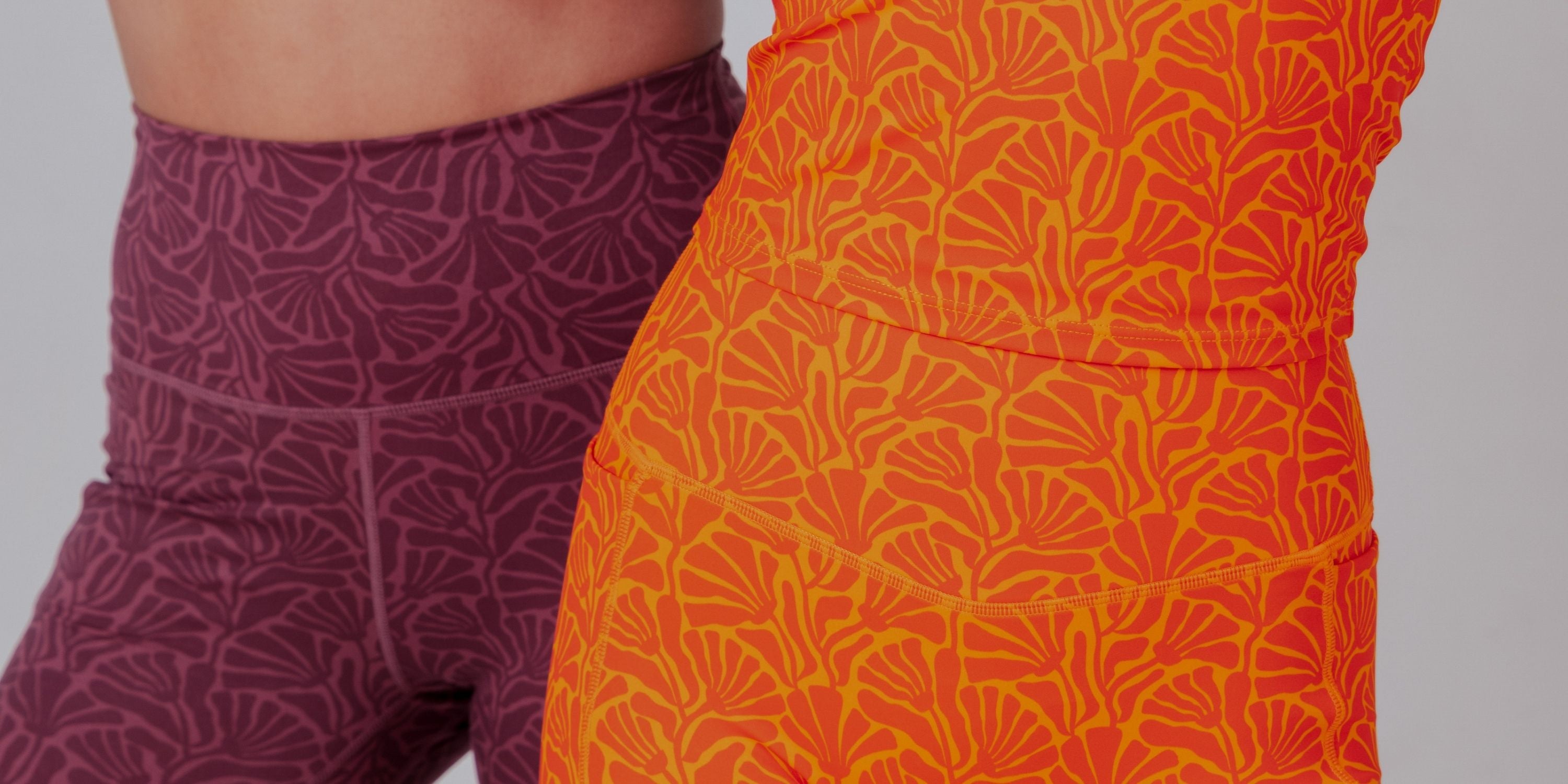 Close-up of two people wearing patterned athletic leggings, one in plum purple and one in bright orange, against a light gray background.